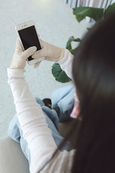 Person wearing gloves holds smartphone indoors, seen from above.