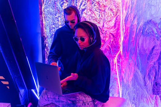 Two individuals in a neon-lit room work on a laptop, showcasing modern technology themes.