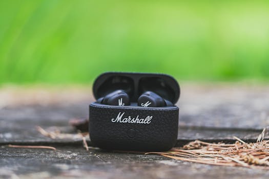 Close-up of Marshall earbuds in case on a wooden surface outdoors with natural greenery.